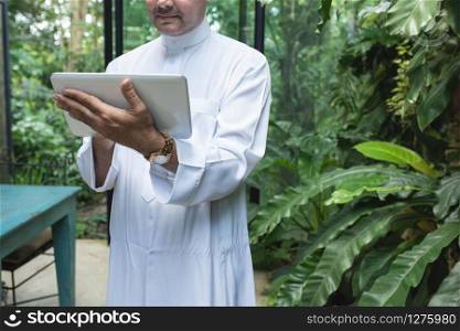 Saudi business asian man using tablet,standing in green cafe wear muslim dress ,freelance business concept.