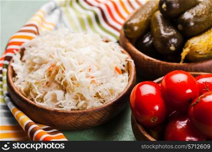 Sauerkraut and pickled cucumbers and tomatoes in wooden bowls