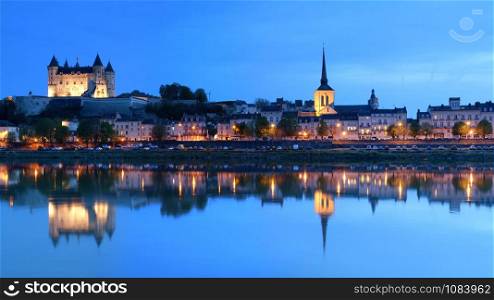 Saumur, France - April 18, 2019: Panorama of Saumur at night with the medieval castle and the old town with Saint-Pierre church, Pays de la Loire, France.