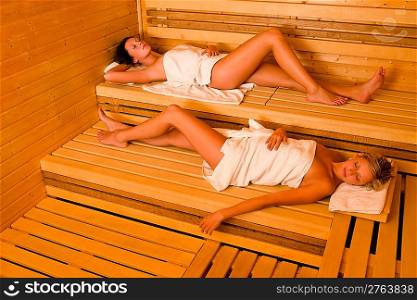 Sauna two healthy beautiful women relaxing lying wrapped in towel
