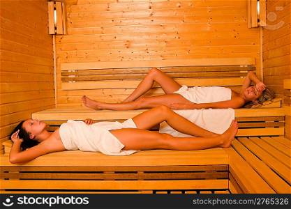 Sauna two healthy beautiful women relaxing lying wrapped in towel