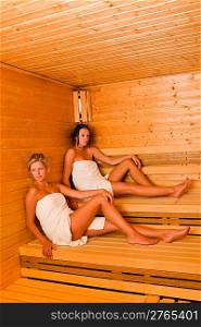 Sauna two healthy beautiful women relaxing sitting wrapped in towel