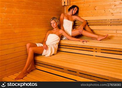 Sauna two healthy beautiful women relaxing sitting wrapped in towel