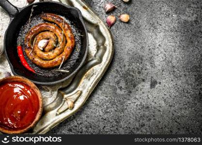 Sausage in a frying pan with hot peppers and garlic. on a steel tray. On a rustic background.. Sausage in a frying pan with hot peppers and garlic. on a steel tray.
