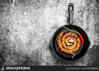 Sausage in a frying pan with hot peppers. On a rustic background.. Sausage in a frying pan with hot peppers.