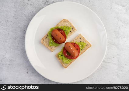 Sausage with tomatoes, salad and two sets of bread on a white plate.