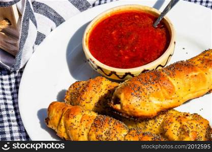 Sausages baked in dough sprinkled with salt and poppy seeds and bowl with tomatoes sauce in a rustic composition. Sausages rolls, delicious homemade pastries.. Sausages baked in dough sprinkled with salt and poppy seeds and bowl with tomatoes sauce in a rustic composition. Sausages rolls, delicious homemade pastries.