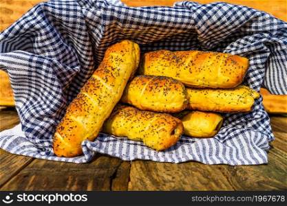Sausages baked in dough sprinkled with salt and poppy seeds in a rustic basket. Sausages rolls, delicious homemade pastries in a rustic composition.. Sausages baked in dough sprinkled with salt and poppy seeds in a rustic basket. Sausages rolls, delicious homemade pastries in a rustic composition.