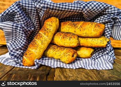 Sausages baked in dough sprinkled with salt and poppy seeds in a rustic basket. Sausages rolls, delicious homemade pastries in a rustic composition.. Sausages baked in dough sprinkled with salt and poppy seeds in a rustic basket. Sausages rolls, delicious homemade pastries in a rustic composition.