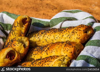 Sausages baked in dough sprinkled with salt and poppy seeds in a rustic basket. Sausages rolls, delicious homemade pastries in a rustic composition.. Sausages baked in dough sprinkled with salt and poppy seeds in a rustic basket. Sausages rolls, delicious homemade pastries in a rustic composition.