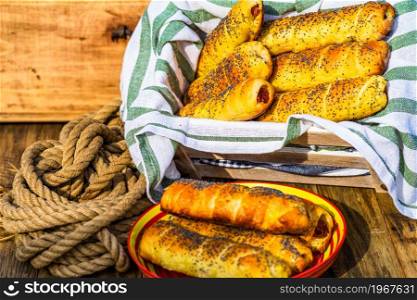 Sausages baked in dough sprinkled with salt and poppy seeds in a rustic composition. Sausages rolls, delicious homemade pastries.. Sausages baked in dough sprinkled with salt and poppy seeds in a rustic composition. Sausages rolls, delicious homemade pastries.