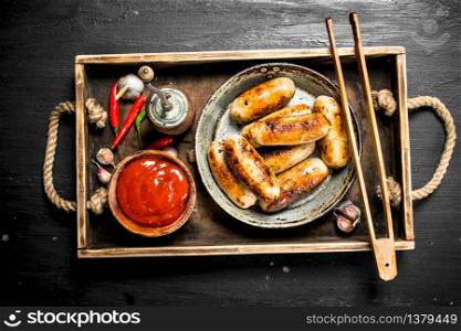 Sausages in a frying pan with sauce on a wooden tray. On the black chalkboard.. Sausages in a frying pan with sauce on a wooden tray.