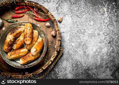 Sausages in an old pan with hot peppers. On a rustic background.. Sausages in an old pan with hot peppers.