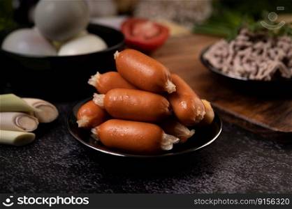 Sausages on a black plate that are placed on the cement floor. Selective focus.