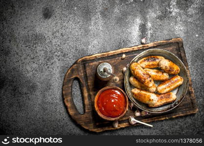 Sausages with tomato sauce on the board. On a rustic background.. Sausages with tomato sauce on the board.