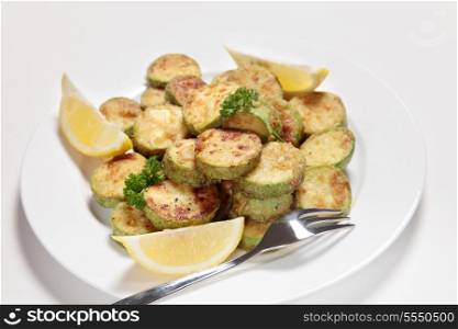 Sauteed courgette (zucchini) slices served with lemon wedges and garnished with parsley. The the courgettes are sliced, tossed in flour and fried in butter or olive oil and then seasoned.