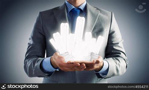 Save energy. Close up of businessman hands holding glass light bulbs