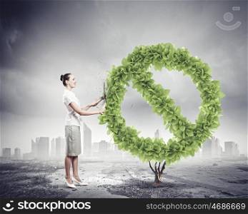Save home. Young businesswoman cutting plant shaped like prohibition sign. Ecology concept