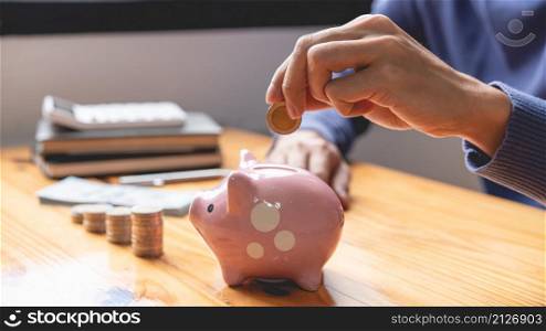 saving concept the male picking his coin to drop it into a pink piggy bank as his money saving up for this month.