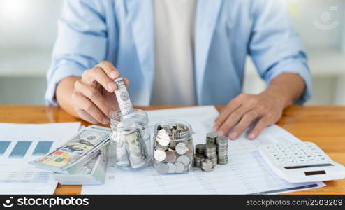 Saving concept the male young adult rolling his cash and putting it into the bottle.