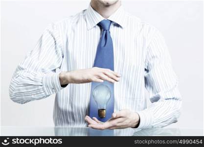 Saving electric energy. Hands of businessman holding with care glass light bulb