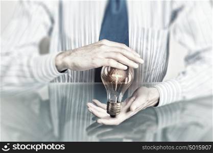 Saving electric energy. Hands of businessman holding with care glass light bulb
