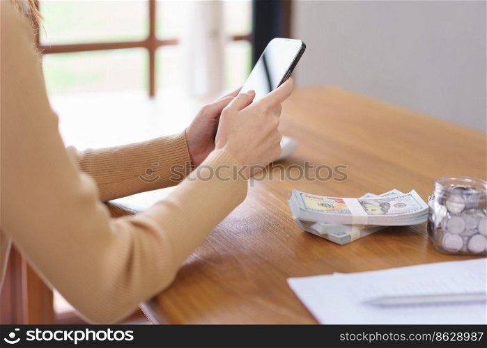 Saving money concept, Asian woman use smartphone and reading data after count the amount of savings.