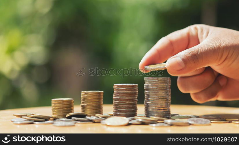 saving money hand putting coins on stack on table with sunshine. concept finance and accounting