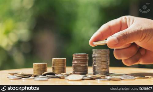 saving money hand putting coins on stack on table with sunshine. concept finance and accounting
