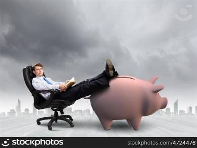 Saving money. Young handsome businessman sitting in chair. Banking concept