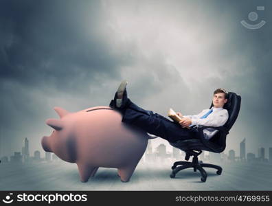 Saving money. Young handsome businessman sitting in chair. Banking concept