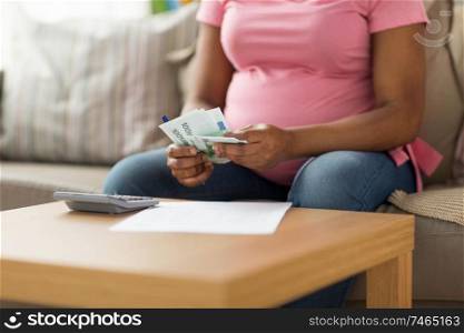 savings, finances and people concept - close up of pregnant african american woman with papers and calculator counting money at home. pregnant woman counting money at home