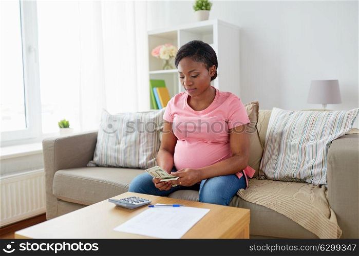 savings, finances and people concept - pregnant african american woman with papers and calculator counting money at home. pregnant woman counting money at home