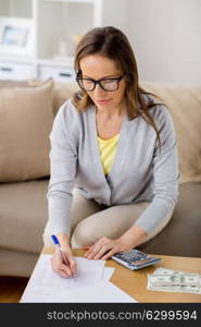 savings, finances, business and people concept - woman with papers and calculator counting money at home. woman with money, papers and calculator at home