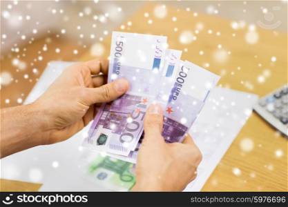 savings, finances, economy and home concept - close up of man hands counting money at home over snow effect
