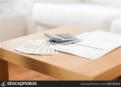 savings, finances, economy and home concept - close up of money with papers and calculator on table at home