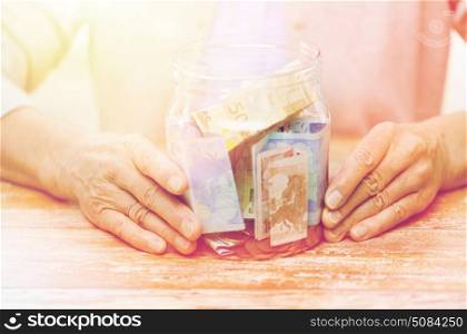 savings, money, annuity insurance, retirement and people concept - close up of senior woman hands with money in glass jar. close up of senior woman with money in glass jar. close up of senior woman with money in glass jar