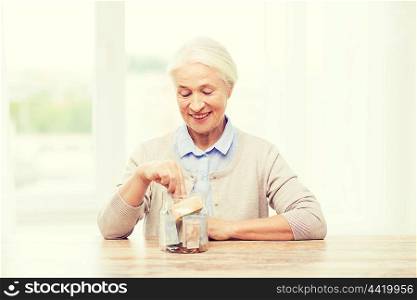 savings, money, annuity insurance, retirement and people concept - smiling senior woman putting bank notes into glass jar at home