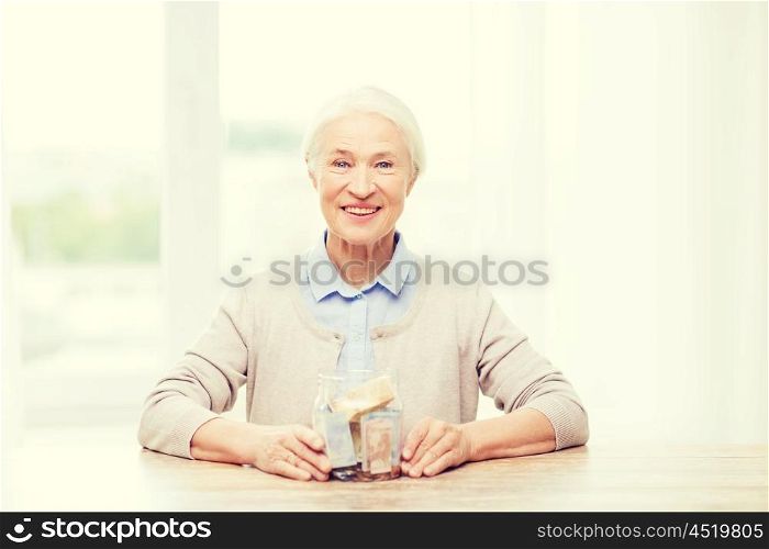 savings, money, annuity insurance, retirement and people concept - smiling senior woman with money in glass jar at home