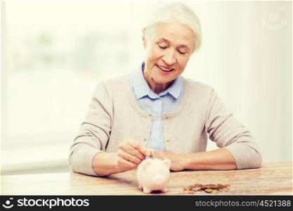 savings, money, annuity insurance, retirement and people concept - smiling senior woman putting coins into piggy bank at home