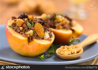 Savory baked apple filled with mincemeat, raisins, sultanas, onion and walnut, sprinkled with fresh thyme leaves on top served on blue plate with walnuts on wooden spoon (Selective Focus, Focus on the sultana in the front)