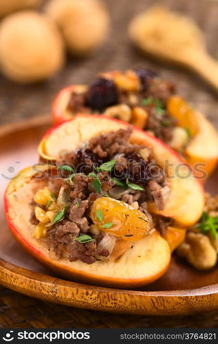 Savory baked apple filled with mincemeat, raisins, sultanas, onion and walnut, sprinkled with fresh thyme leaves on top with walnuts in the back (Selective Focus, Focus on the filling in the front)