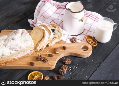 Savory breakfast with sliced pound cake, surrounded by roasted nuts and dried orange, near a bucket of fresh milk, on a vintage wooden table.