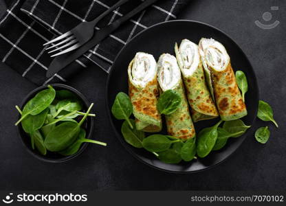 Savory crepes with spinach and feta cheese on black background, top view