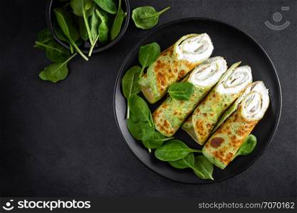 Savory crepes with spinach and feta cheese on black background, top view