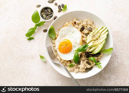 Savory oatmeal with fried sunny side up egg, avocado and pumpkin seeds for healthy breakfast