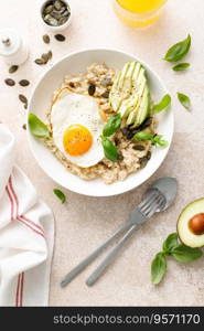 Savory oatmeal with fried sunny side up egg, avocado and pumpkin seeds for healthy breakfast