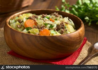 Savoy cabbage, carrot, potato and mincemeat stew or thick soup with parsley in wooden bowl, photographed on dark wood with natural light (Selective Focus, Focus in the middle of the dish)