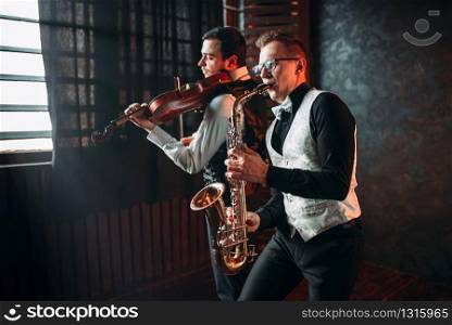 Sax man and fiddler duet playing classical melody. Jazz man and violinist. Sax man and fiddler duet playing classical melody