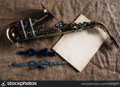 Saxophone, notes and bowtie on grunge canvas background, closeup view. Brass band instrument concept. Classical sax, jazz music